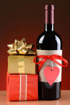 Closeup of a wine bottle decorated for Valentines Day. A stack of presents are next to the bottle. The bottle has a red ribbon and heart shaped tag and a blank label.
