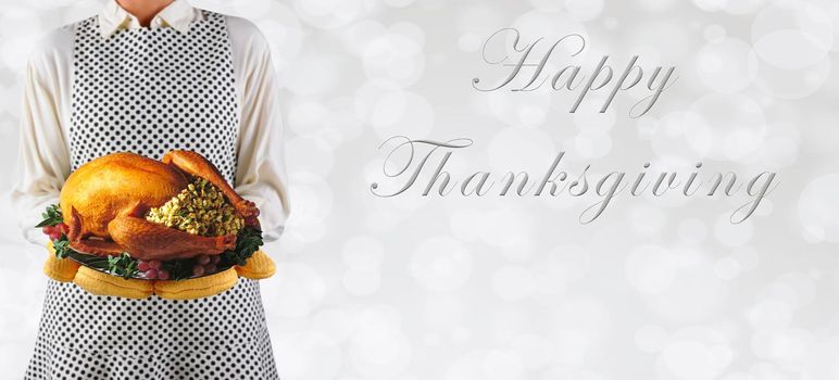 Woman holding a Thanksgiving turkey on a platter over a silver bokeh background, with Happy Thanksgiving and copy space.