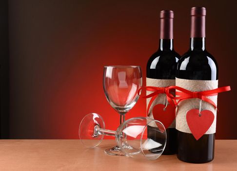 Closeup of a wine bottles decorated for Valentines Day. Two empty wineglasses are next to the bottles with one on its side.  Both bottles have a red ribbon and heart shaped tag and a blank label.