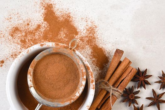 Flay lay arrangement of Cinnamon and Star Anise on a light gray table. Powdered spice, sticks bundled with twine and a sifter with copy space.