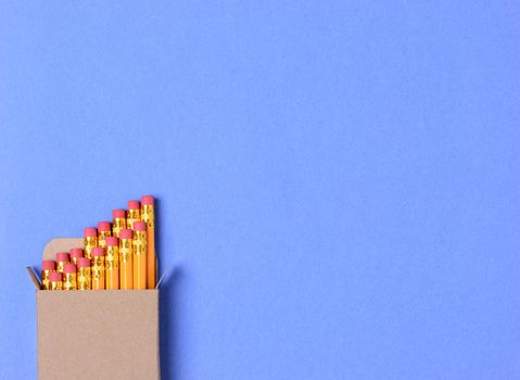 High angle shot of a box of new yellow pencils on a blue construction paper background. Horizontal format with copy space. Perfect for Back to School concepts.