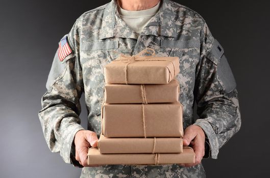 Closeup of a soldier wearing camouflage fatigues holding a stack of packages for mail call. Horizontal format, man is unrecognizable.