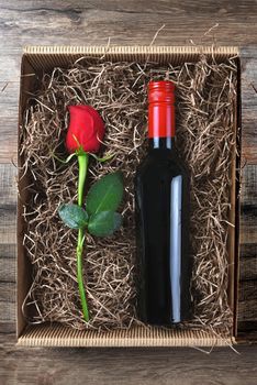 A single red rose and a bottle of wine in a cardboard box filled with packing material. High angle shot. Valentines / Love / Romance Concept.
