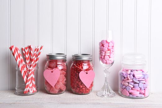 Valentines Day candy in a variety of glass containers on white wood.