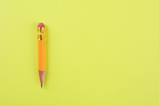 Overhead closeup of a sharpened pencil stub on a yellow background. The well used #2 pencil is set ot the left side of the frame, leaving copy space.