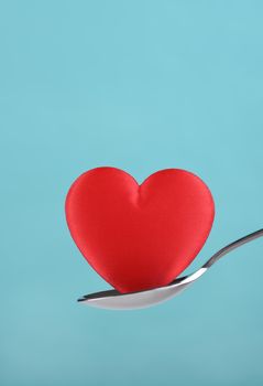 Red heart balanced on a spoon against a teal background.