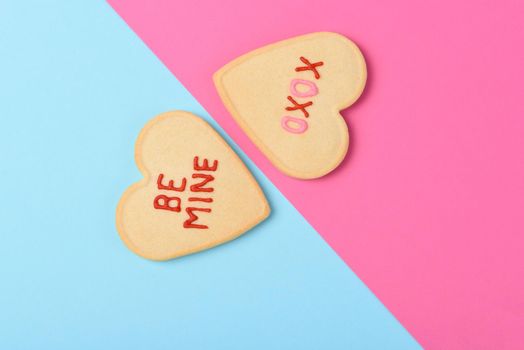 Valentines Day Concept: Two Heart shaped sugar cookies one on pink one on blue with Be Mine and XOXO written in icing. 