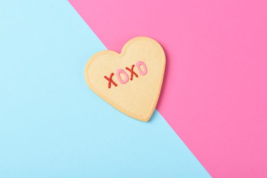 Valentines Day Concept: A Heart shaped sugar cookie on pink and blue with XOXO written in pink and red icing, and copy space.