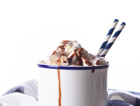 Closeup of a white mug of hot chocolate with whipped cream and two paper drinking straws. 