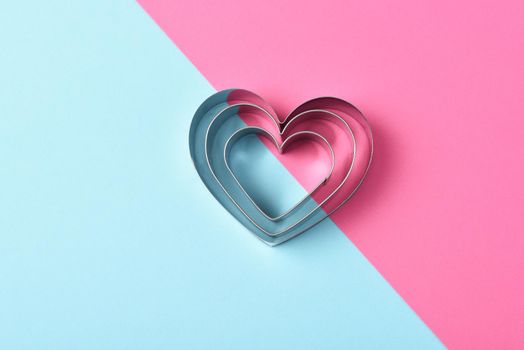 Valentines Day Concept: Nested Heart shaped cookie cutters on pink and blue with copy space.