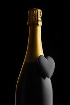 Valentines Day Concept: Closeup of a bottle of Champagne with a black heart against a black background.
