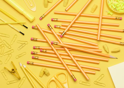 Yellow School Supplies. Pencils, erasers, paper clips, brushes, pins, scissors, paper laying in a random pattern on a yellow background. Closeup filling the frame with everything in a shade of yellow..