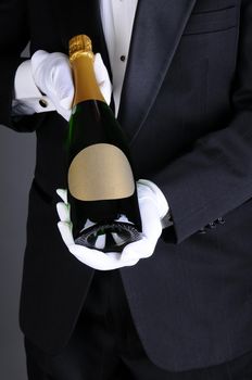 Closeup of a Sommelier in a tuxedo presenting a champagne bottle, Vertical format over a light to dark gray background. Man is unrecognizable.