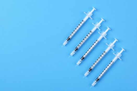 Five new syringes on a blue background with copy space.