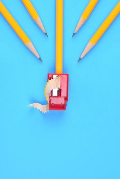 Back to School Concept: Four Yellow Pencils pointing to a sharpener and shavings, on a blue background. Copy space at bottom.