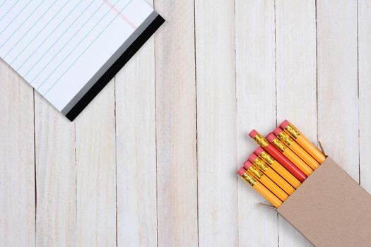 High angle shot of a box of pencils and a writing tablet on a white wood surface. Objects are in opposite corners of the frame.