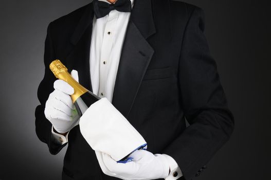 Closeup of a Sommelier holding a Champagne bottle in front of his torso. Man is unrecognizable. Horizontal format on a light to dark gray background.