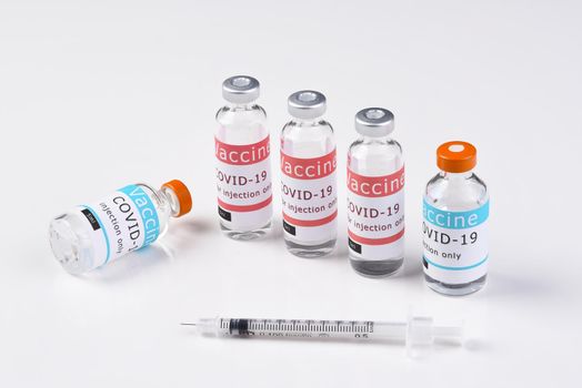 Two different types of Covid-19 Vaccines on white with a syringe in the foreground.