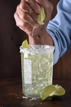 Closeup of a bartender squeezing a line into a drink glass with a salt encrusted rim. 