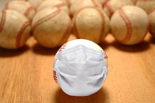 Sports and COVID-19 Concept. A new baseball with a surgical mask in front of a group of out of focus old balls without masks.