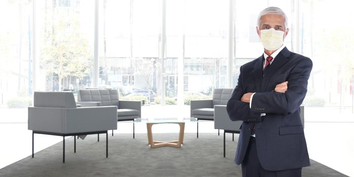 Businessman standing in empty office without customers or employees wearing his COVID-19 mask practicing social distancing. Wide format with copy space, 