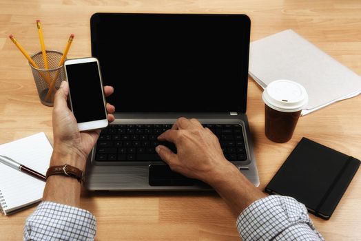 Cropped high angle shot of a businessman using a computer and cell phone while working at home.