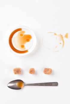 Top view of a coffee stain with plastic lid a spoon and sugar cubes on white paper. Vertical format with copy space.