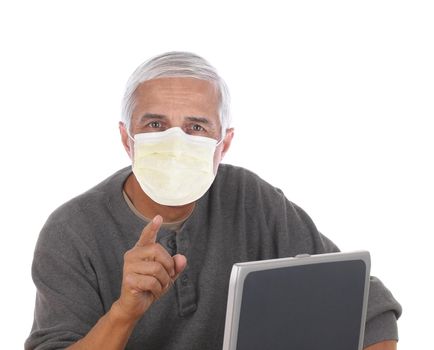 Casual middle aged man wearing a covid-19 protective mask sitting at laptop computer and pointing at camera. Horizontal format isolated on white.