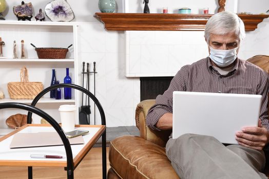 Mature man wearing a surgical mask working from home with his laptop and cell phone during the COVID-19 stay at home restrictions.