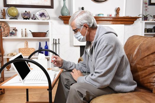 Man not feeling well wearing a COVID-19 face mask checking his temperature on a thermometer, ready to video chat with his health provider or doctor.