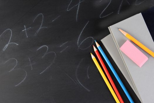 Overhead shot of two text books with colored pencils and an eraser on a partially erased blackboard. Horizontal format with copy space.