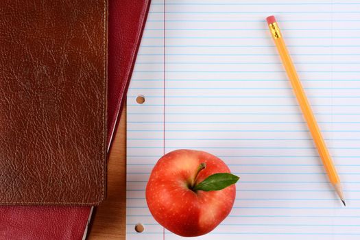 Overhead view of an apple  and pencil on notebook paper with school books. Closeup in horizontal format. Back to School concept.