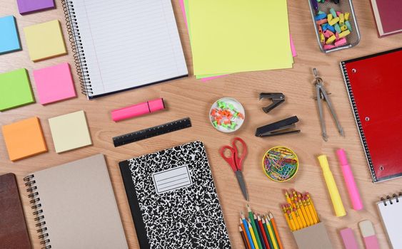 High angle shot of school supplies laid out on a wood desk. Back to School concept with paper, pads, pencils, notebooks, scissors, erasers and more. Horizontal format at an angle.