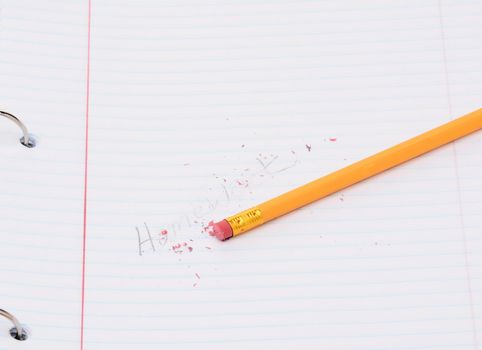 Closeup of a pencil on a notebook page with the word homework partially erased. Back to school concept. 