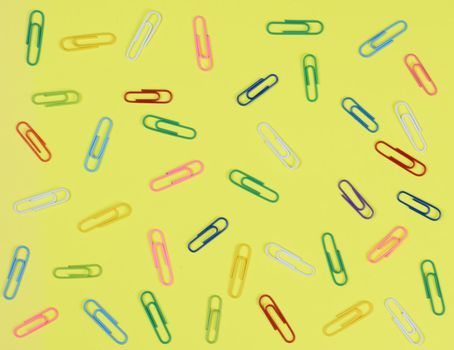 A group of multi-colored paper clips spread out on a yellow background.