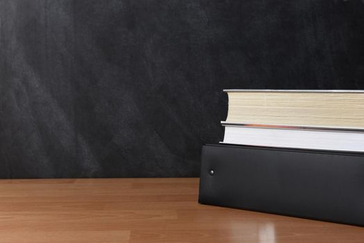 A binder with two textbooks on a teachers desk in front of a chalkboard.