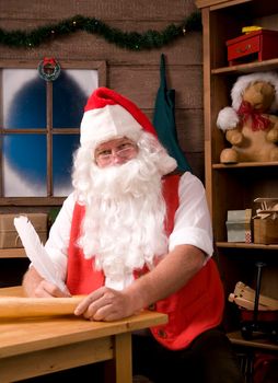 Santa Claus Sitting in His Workshop with Quill Pen Writing on His List. Vertical Composition.