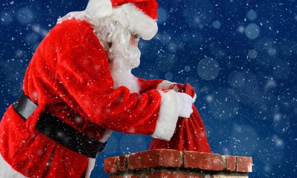 Closeup of Santa Claus placing his bag of toys into a chimney with snow flakes blue Bokeh background.

