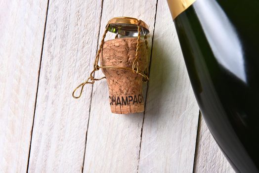 Top view of a bottle of champagne next to a cork on a rustic white wood table. Horizontal format with copy space.