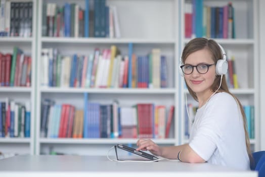 female student study in school library, using tablet and searching for information’s on internet. Listening music and lessons on white headphones