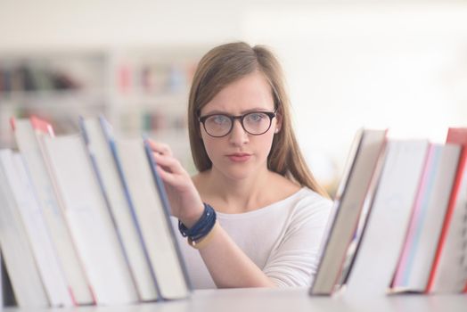 portrait of smart looking famale student girl  in collage school library,  selecting book to read from bookshelf