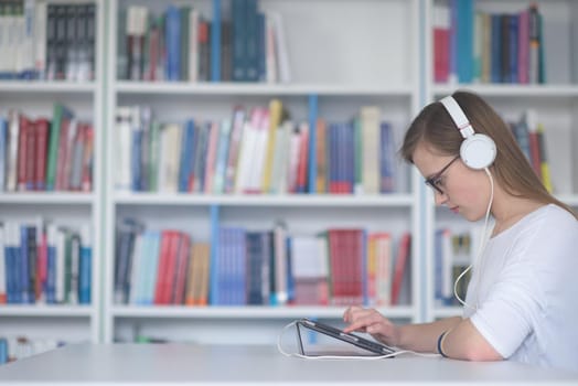 female student study in school library, using tablet and searching for information’s on internet. Listening music and lessons on white headphones