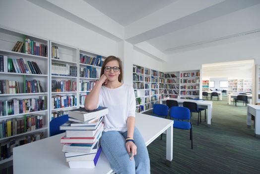 female student study in school library, using tablet and searching for information’s on internet. Listening music and lessons on white headphones