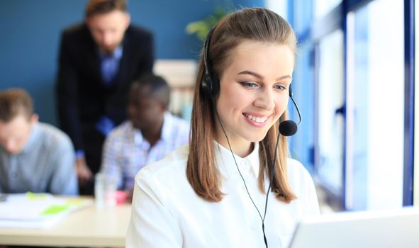 Portrait of call center worker accompanied by her team. Smiling customer support operator at work.