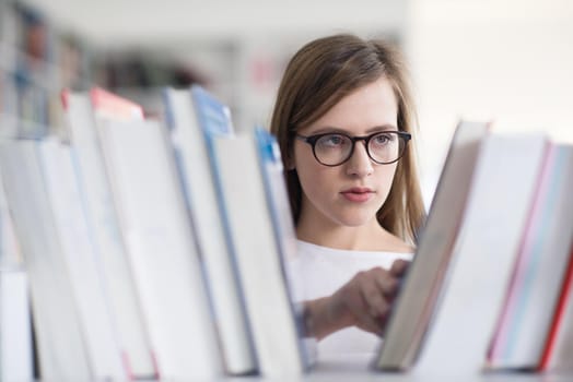 portrait of smart looking famale student girl  in collage school library,  selecting book to read from bookshelf