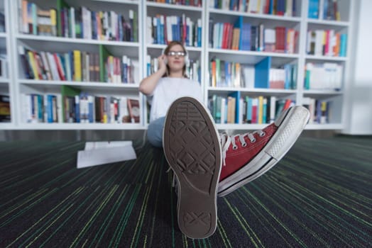 female student study in school library, using tablet and searching for information’s on internet. Listening music and lessons on white headphones