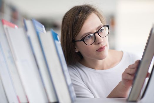 portrait of smart looking famale student girl  in collage school library,  selecting book to read from bookshelf