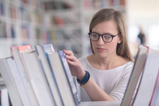 portrait of smart looking famale student girl  in collage school library,  selecting book to read from bookshelf