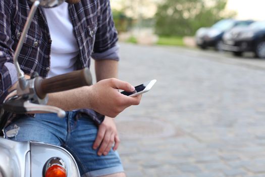 Young man sitting on scooter and using smart phone