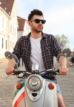 fashionable young man riding a vintage scooter in the street